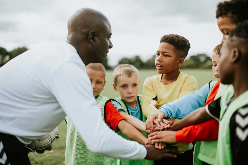 Soccer trainer with kids standing in a circle on a sport field