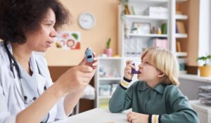 Side view portrait of female pediatrician teaching little boy using inhaler at doctors office