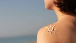 A woman standing on a sunny beach with sunscreen applied to her back in the shape of a sun for summer skin care