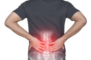 A person holding their lower back in pain, with an overlay of a spinal X-ray and red highlight indicating discomfort or injury in the lumbar region.