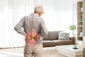 Older man holding his lower back in pain, with an illustrated spine highlighting the affected area, representing back pain.