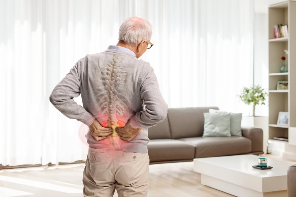 Older man holding his lower back in pain, with an illustrated spine highlighting the affected area, representing back pain.