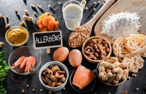 Various common ingredients that can cause food allergies, including milk, eggs, peanuts, tree nuts, seafood, wheat, soy, and mustard, displayed with a chalkboard sign labeled 'Allergens'.